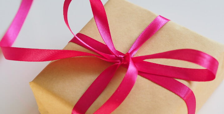Photo of a small present, wrapped in yellow plain paper and a pink ribbon tidied into a bow