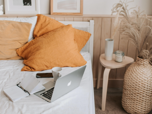 A laptop, notebook and coffee on a bed