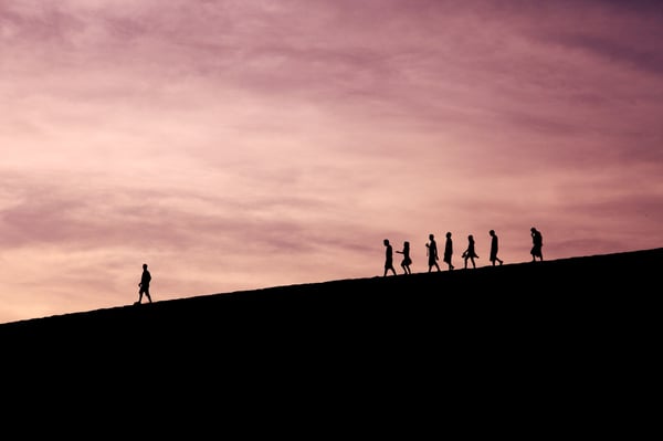 group of people walking in a line with one person walking ahead on their own