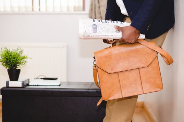 a person leaning against a wall holding a newspaper and bag