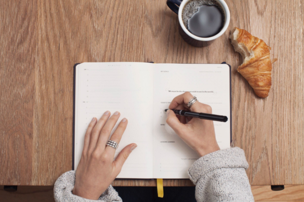 Someone writing in a book having a coffee