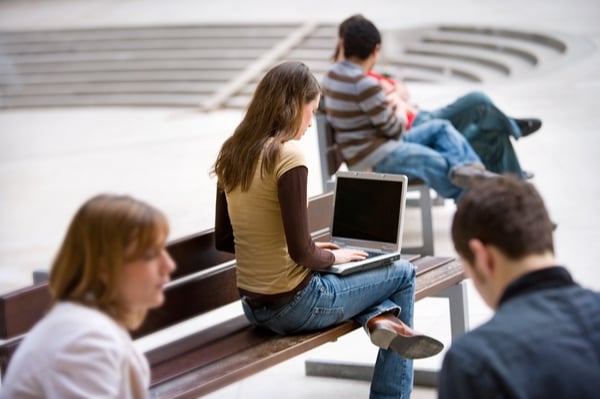 A girl sitting on a bench and writing on her laptop