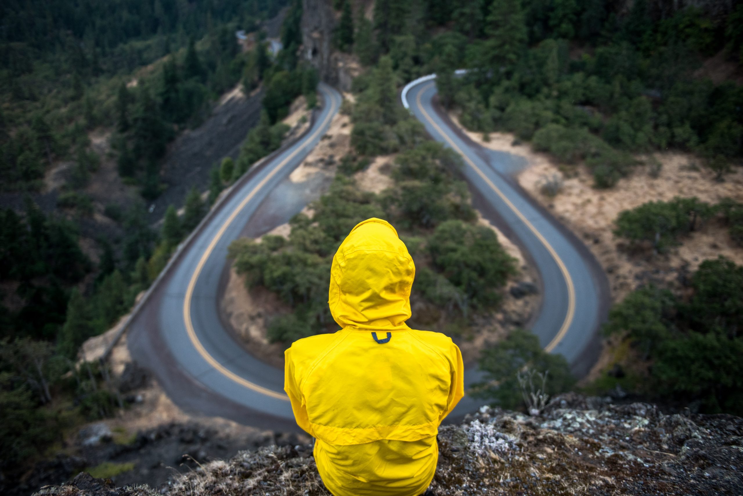 Person in yellow jacket sitting on a cliff overlooking a road