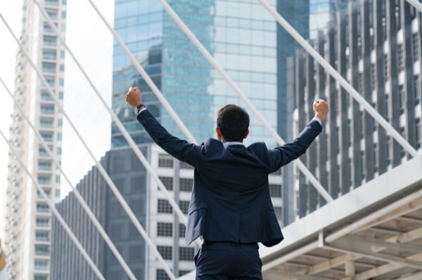 man holding arms up in front of skyscraper