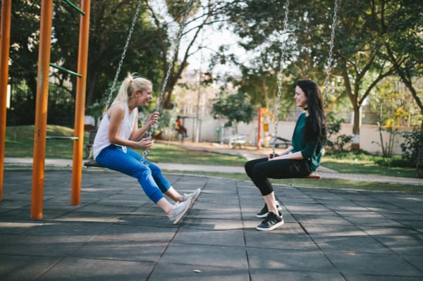 two women sitting on swings facing each other
