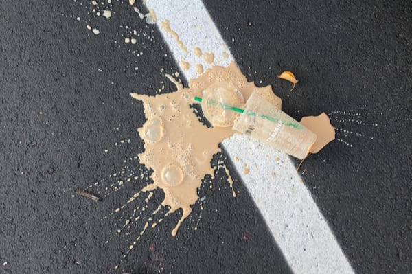 Plastic cup of coffee with a straw dropped on the floor