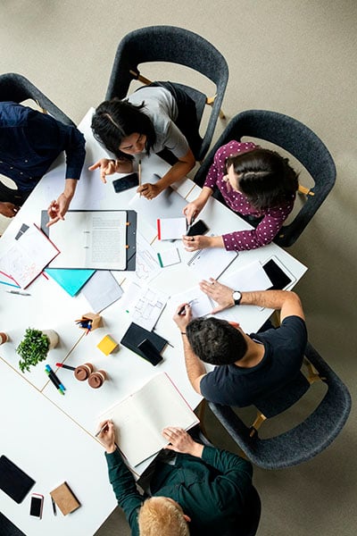 Top view shot of business colleagues discussing over a new project in office. Group of young men and woman brainstorming around table while working on new project.