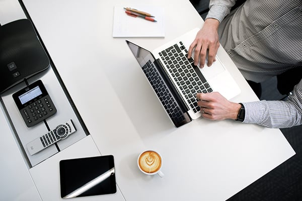 Person using their laptop on a desk with a notepad and pen