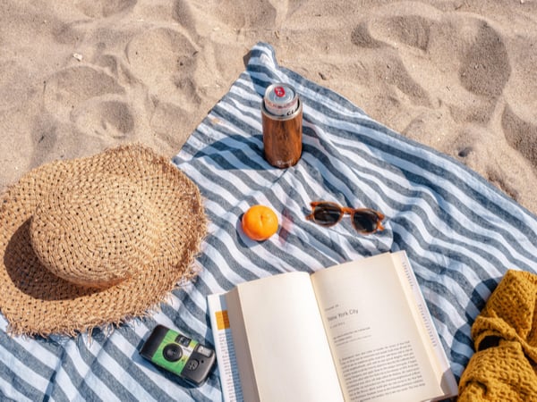 Beach towel on the sand, with a hat, book and sunglasses