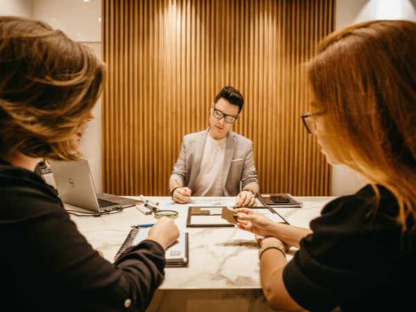 Three people sat in negotiation meeting across a desk