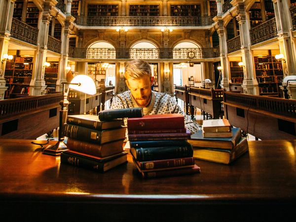 Student learning in library with piles of books