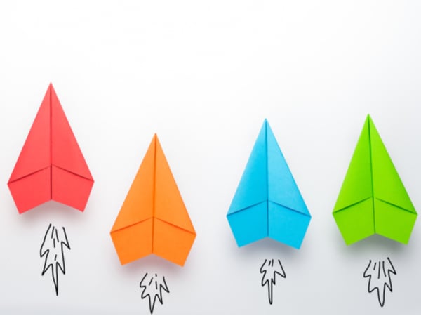 Four different-coloured paper aeroplanes against a white background