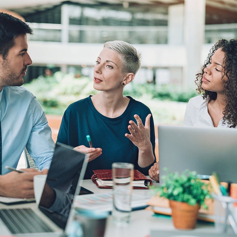 Office workers at desk with laptops in discussion