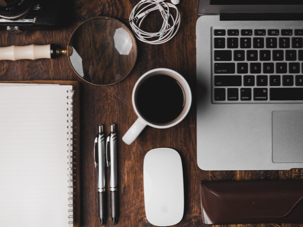 Desk from above: with coffee, laptop, pens, mouse, notebook