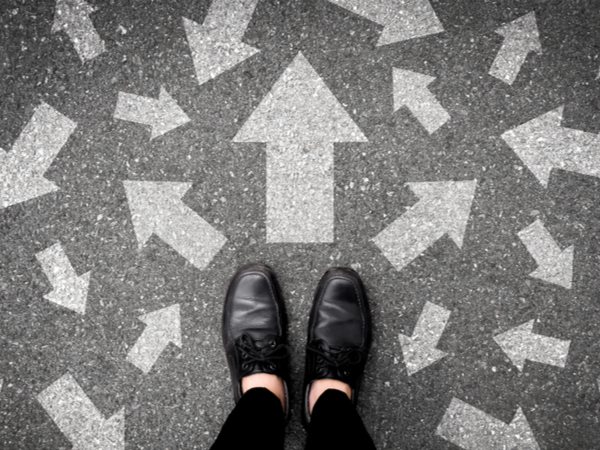 Looking down at feet with many arrows painted on the ground in all directions