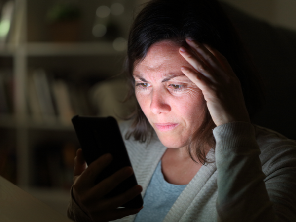 Person's face illuminated by phone screen, looking sad