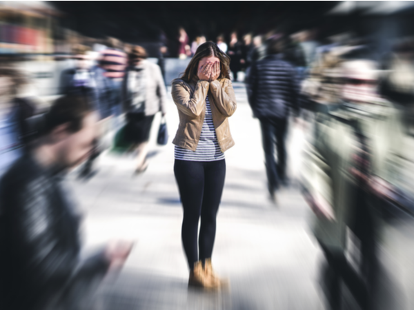 Person with head in their hands surrounded by blurred people walking
