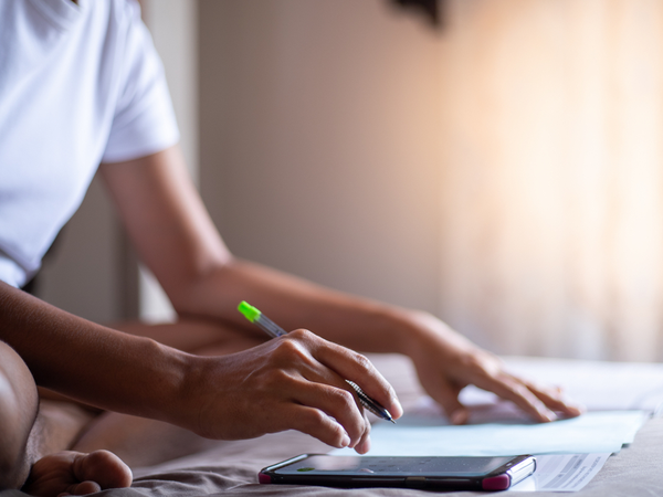 Person working with highlighter and calculator on their bed