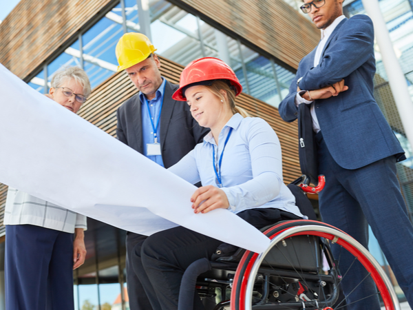 Woman in a wheelchair showing blueprints to colleagues
