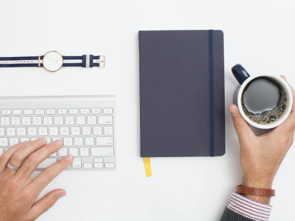 Bird's eye view of a mug of coffee, notebook, keyboard and watch