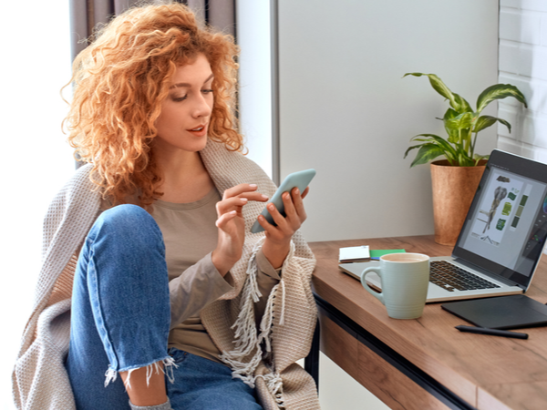 Woman at a desk, multitasking on her laptop and her phone