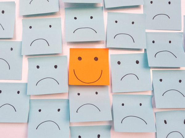 Yellow post-it note with smiley face, surrounded by blue post-its with sad facese