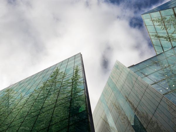 Looking up at tall glass buildings with trees in the reflections