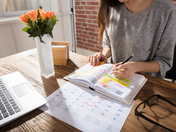 Person writing in a personal planner, looking at a calendar