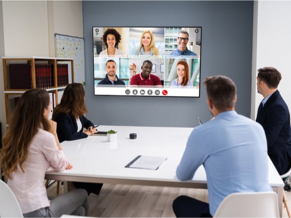 A group of business people sat in a meeting room talking to colleagues on a screen in front of them
