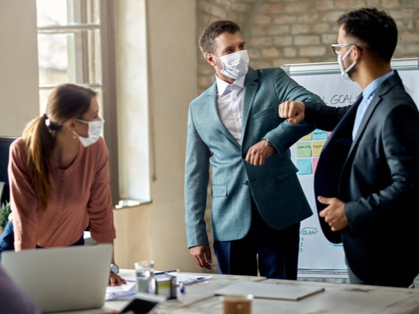 Business coworkers elbow bumping while wearing protective face masks