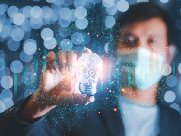 A man in a facemark holding a lit-up lightbulb