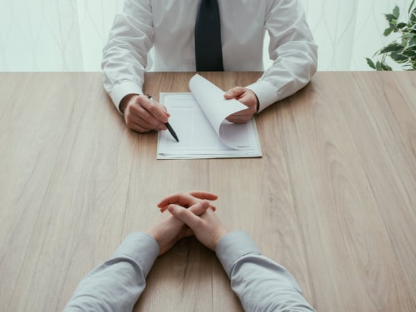 An interviewer reading a CV sitting across the table from a candidate