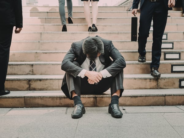 An image of a man sitting alone on some stairs with his head hanging down