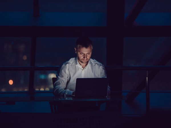 A man working alone on a laptop in the dark at home
