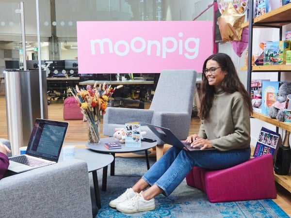 An image of an employee with a laptop sitting in Moonpig's offices