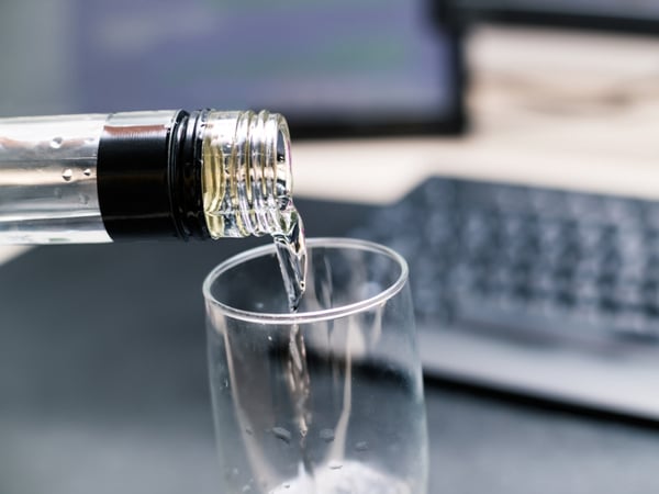 An image of vodka being poured into a glass with a computer keyboard in the background