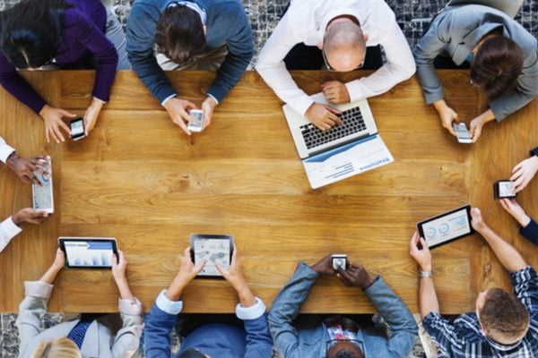 An overhead view of people using laptops and tablets sitting around a large table