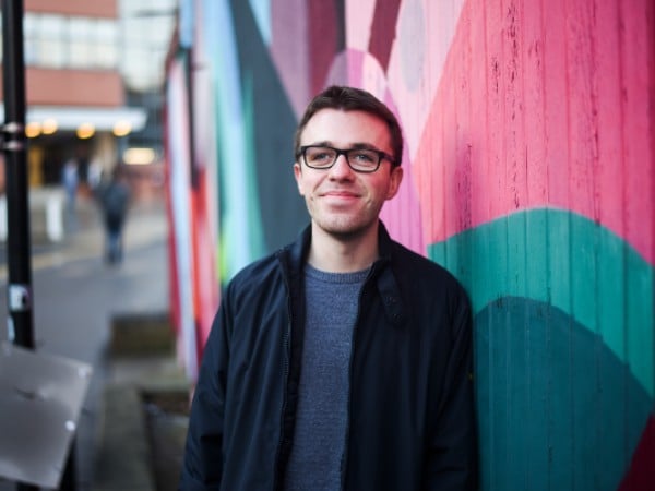 A headshot of Harvey Morton standing in front of a colourful wall