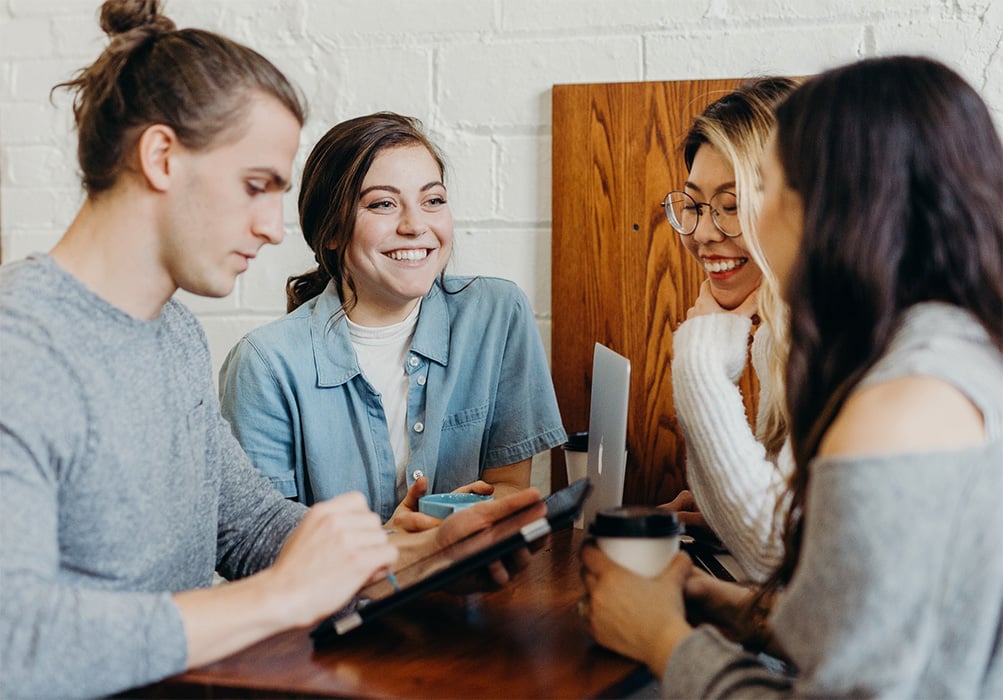 A group of young people around a table with drinks and devices