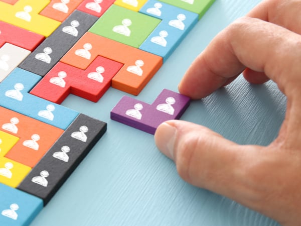 A hand slotting a purple piece with a person icon on it into a multi-coloured jigsaw