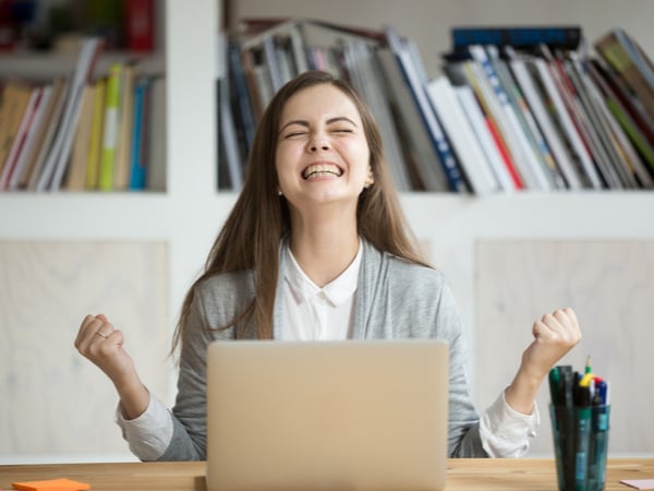 A student celebrating in front of a laptop