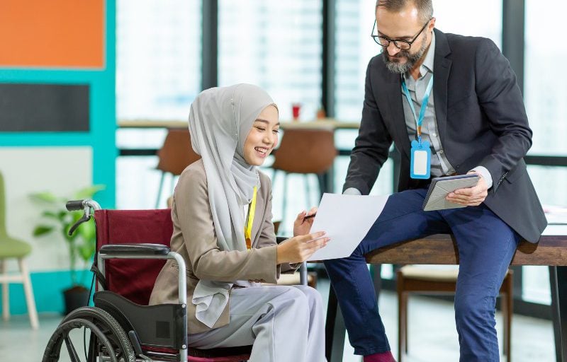 A woman in a wheelchair showing a piece of paper to a man in a suit