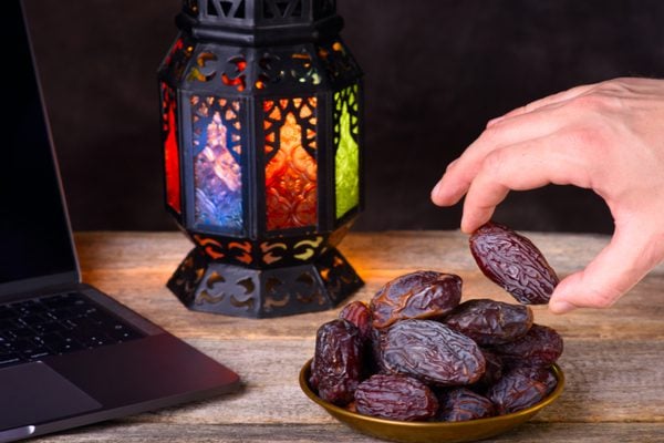 A laptop, a lantern and a hand picking a date from a bowl