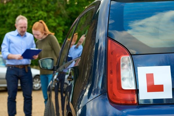 A driving examiner and student standing next to a car with an L plate