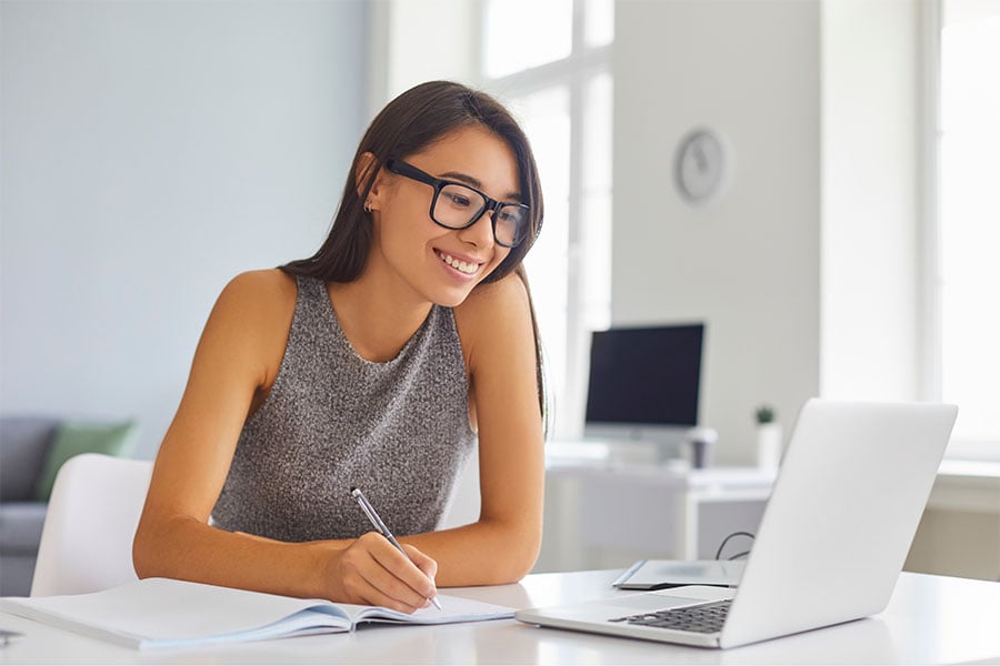 Lady working at desk with pen, paper and laptop