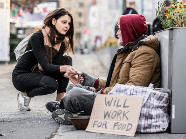 Young woman giving money to homeless man sitting in city