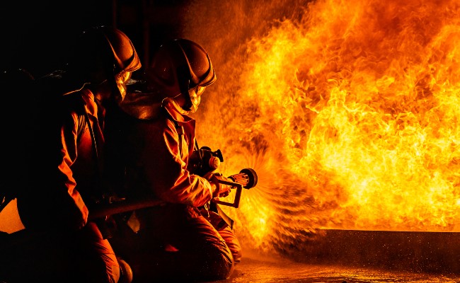 Two firefighters spraying water through a hose on a large fire