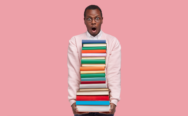 A shocked man holding a large pile of books