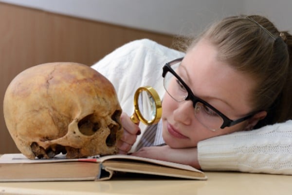 A woman looking at a human skull through a magnifying glass