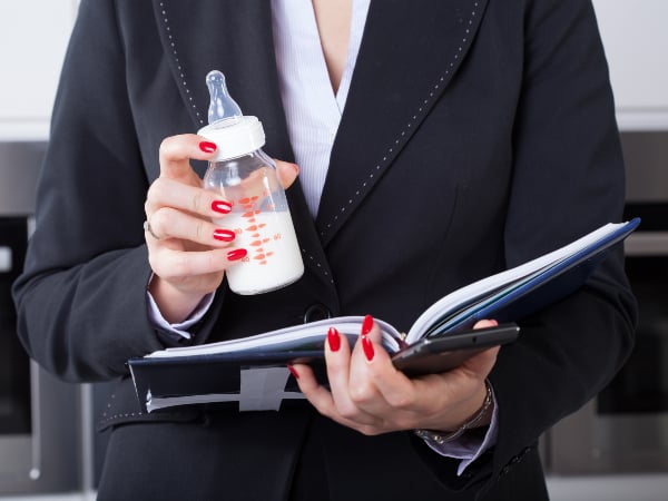 A businesswoman holding a baby bottle and a notebook